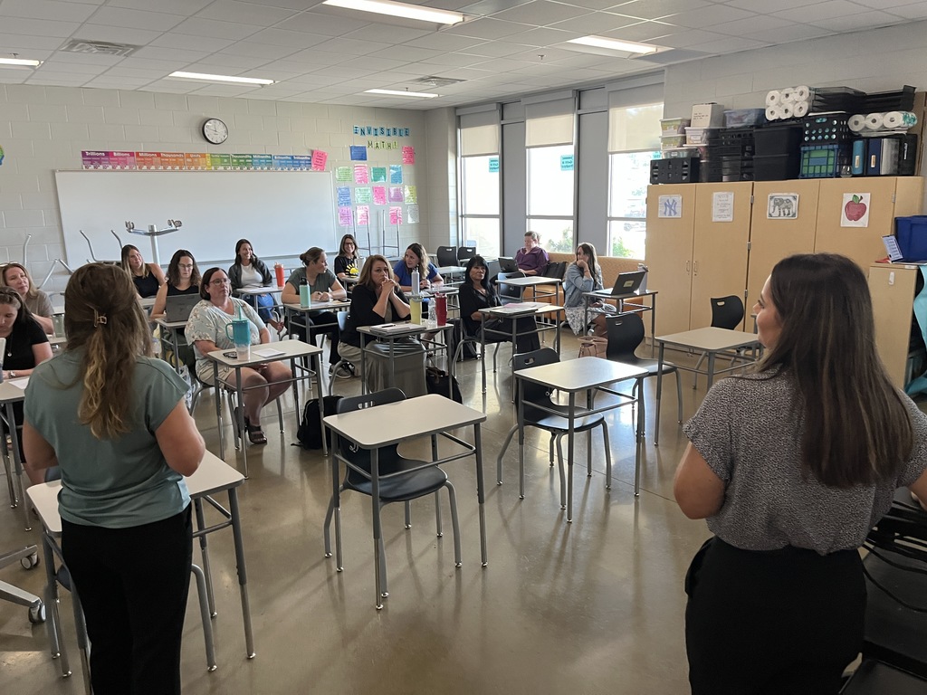 Staff members sitting at tables listen to a speaker during a professional development seminar. 