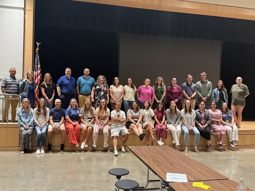 A group of teachers stand and sit on a stage for a group photo.