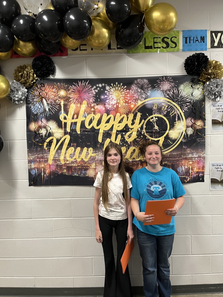 Two students pose for a photo in front of a Happy New Year sign.