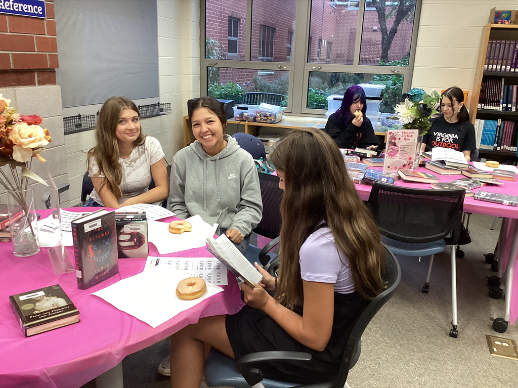 Students sitting at tables full of books participate in a book tasting. 