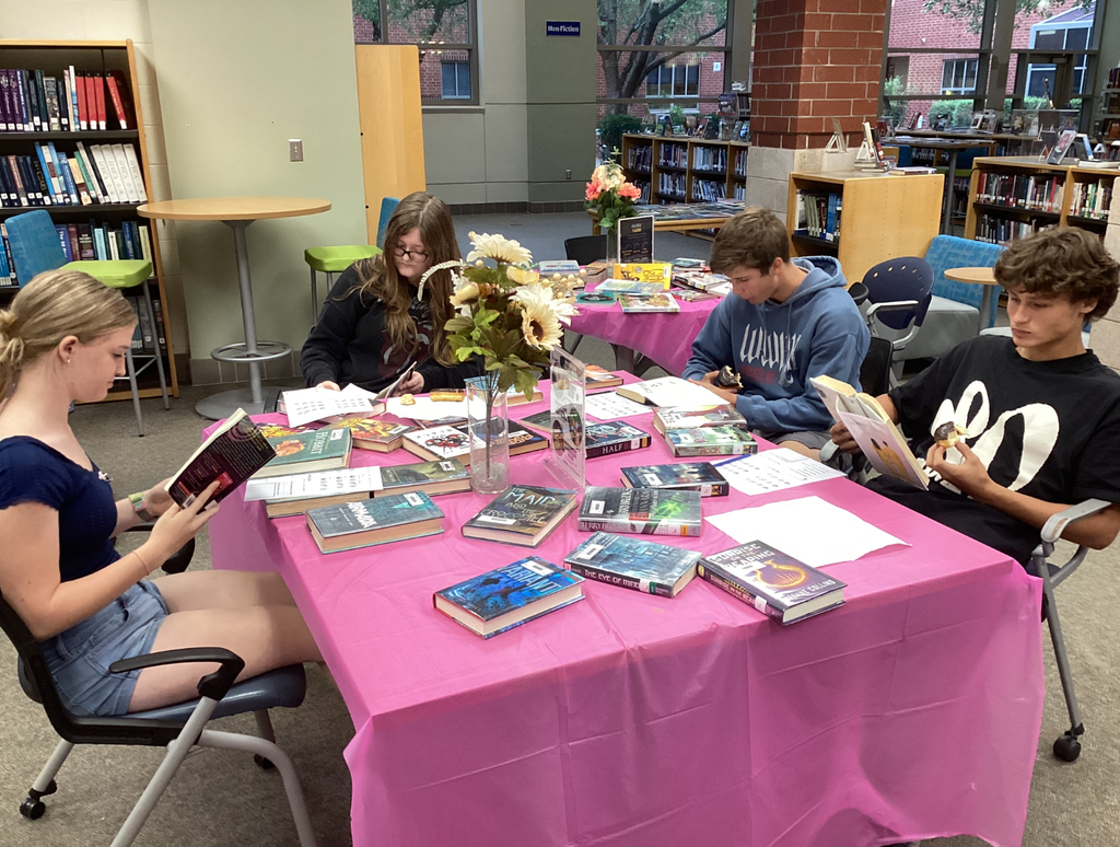 Students sitting at tables full of books participate in a book tasting.  