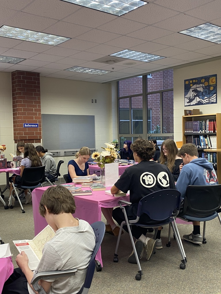 Students sitting at tables full of books participate in a book tasting. 