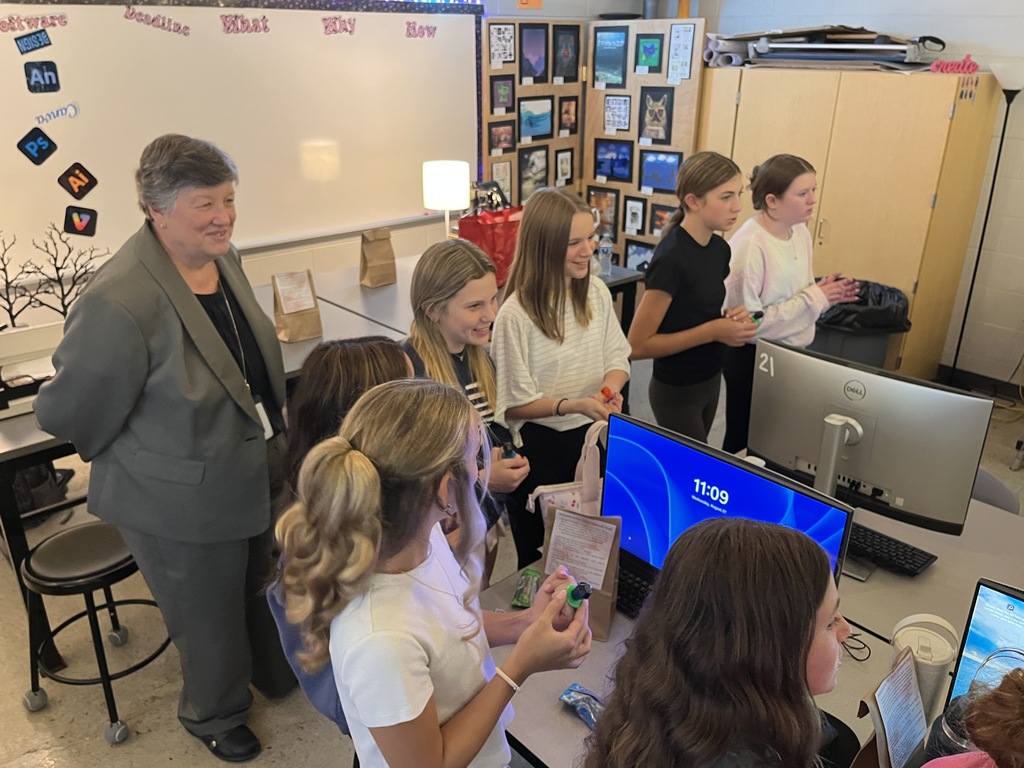 A yearbook teacher leads her students in a yearbook commitment ceremony.  An adult observes. 