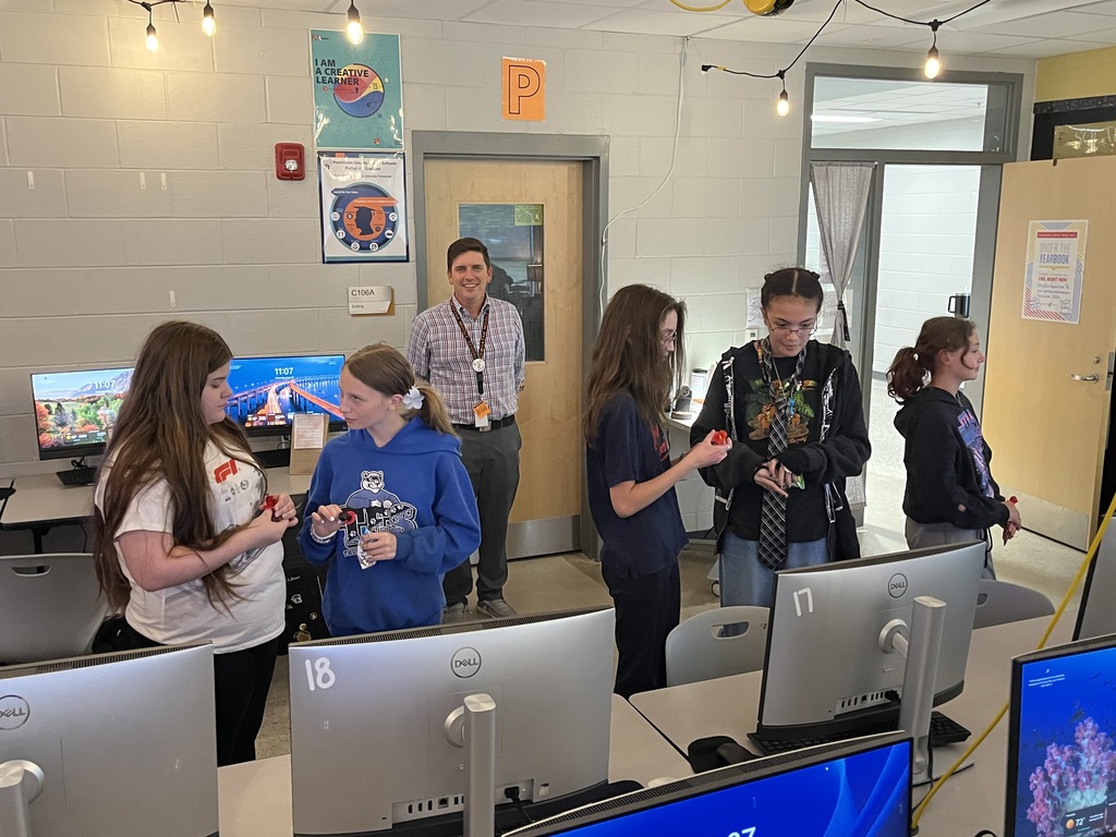 A yearbook teacher leads her students in a yearbook commitment ceremony.  An adult observes. 