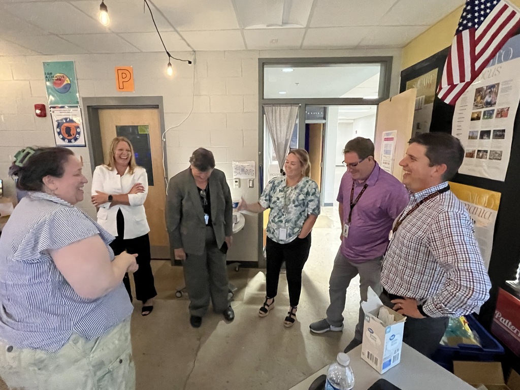 A group of six adults in a semi circle talk and laugh. 