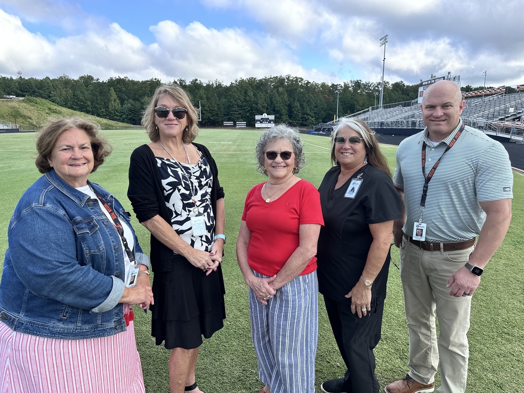 Five people pose for a photo on a football field. 