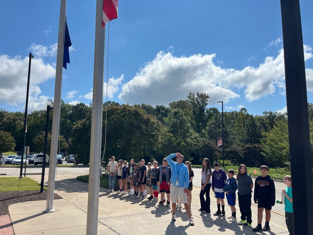 A group of students and a teacher gather at a flagpole on Patriot Day.