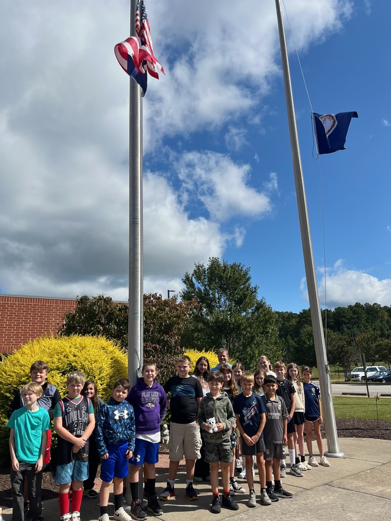 A group of students and a teacher gather at a flagpole on Patriot Day.