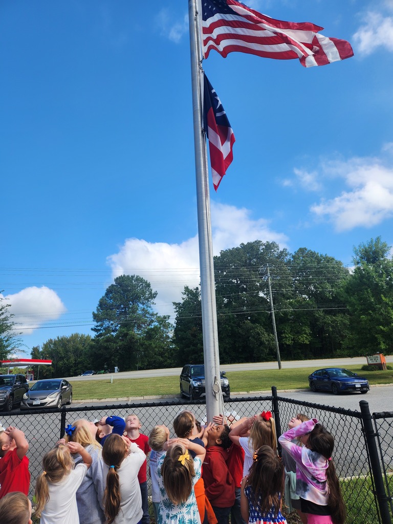 A group of students and a teacher gather at a flagpole on Patriot Day.