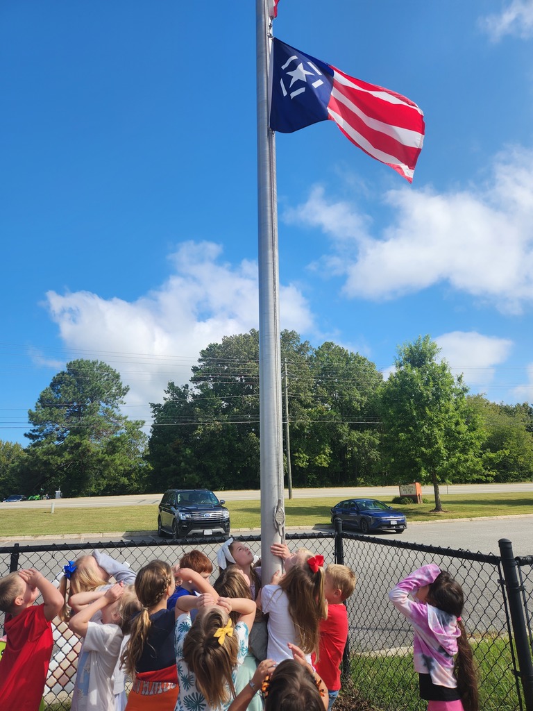 A group of students and a teacher gather at a flagpole on Patriot Day.