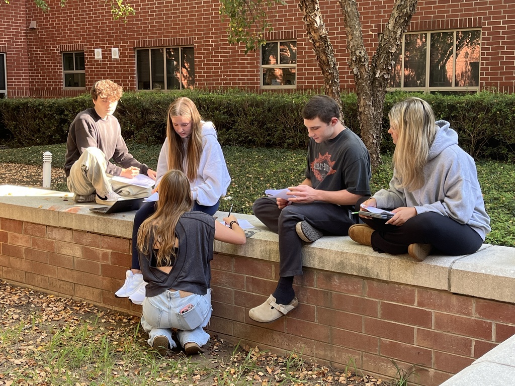 Students working outdoors in a courtyard work on a study guide.