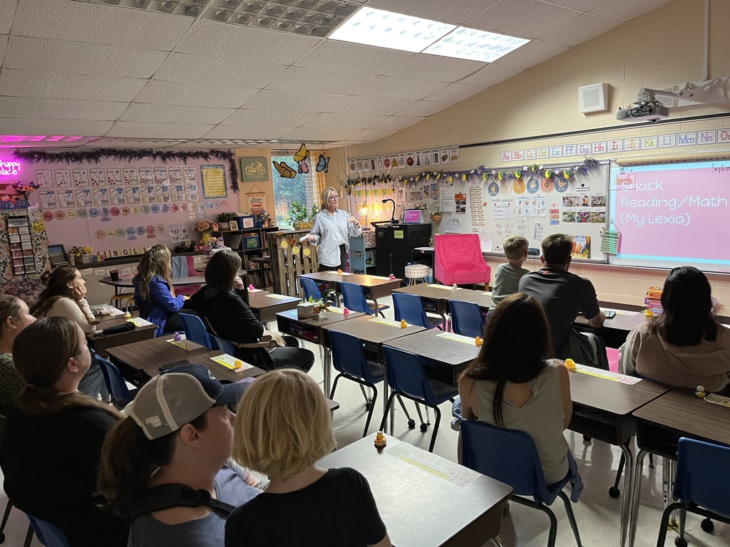 A teacher talks to a classroom full of adults and children on a back-to-school-night.