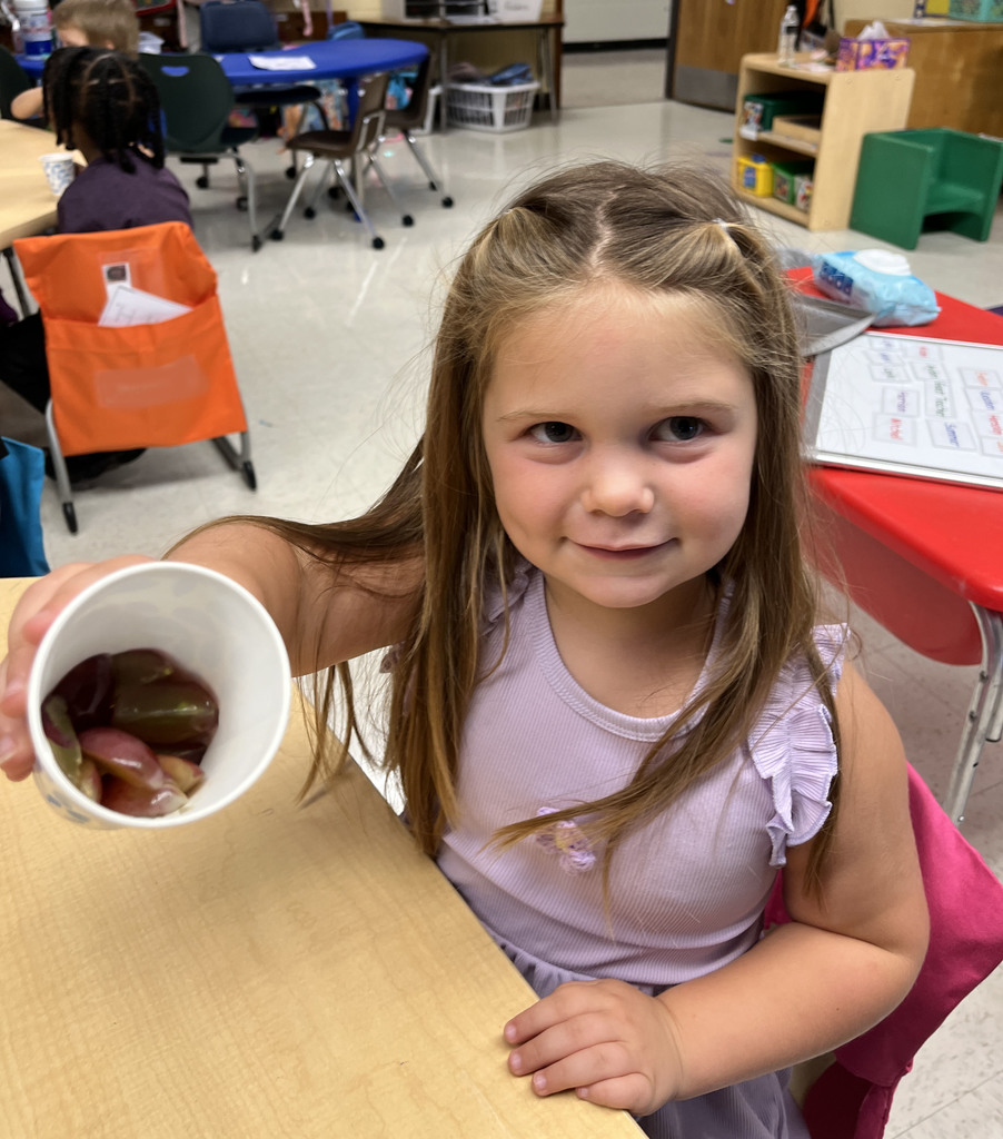 A preschooler enjoys grapes as the snack for purple day.