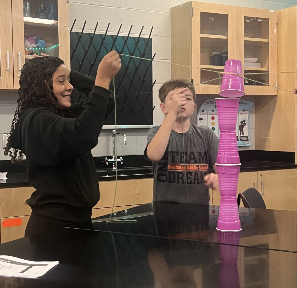 Students cooperate to stack cups using strings as part of a team-building exercise.