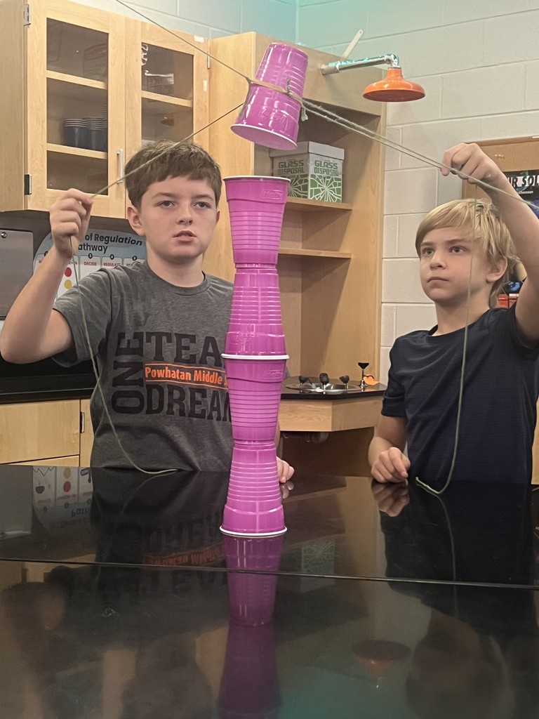 Students cooperate to stack cups using strings as part of a team-building exercise.