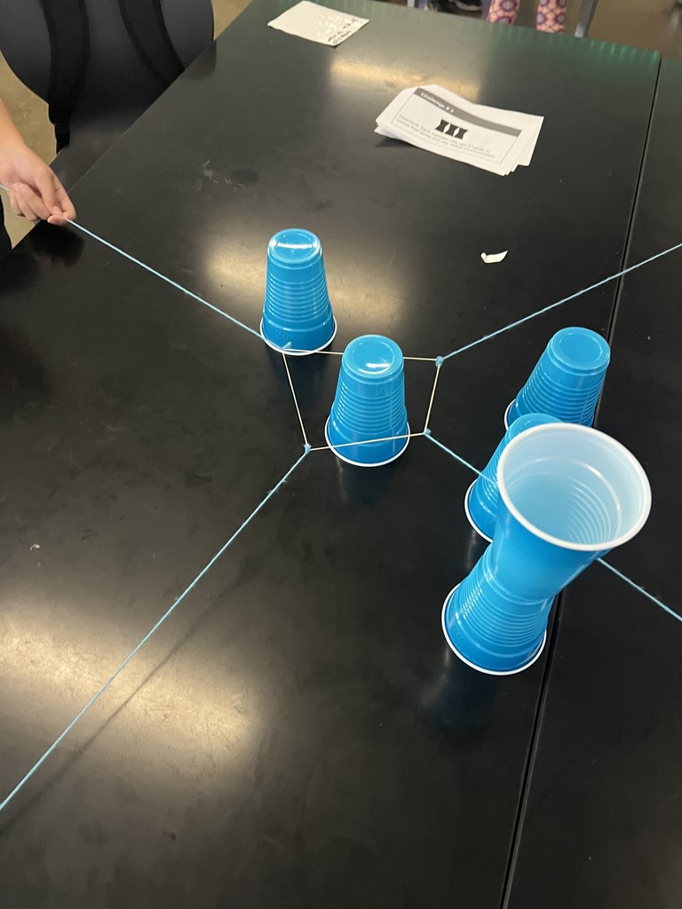 Students cooperate to stack cups using strings as part of a team-building exercise.