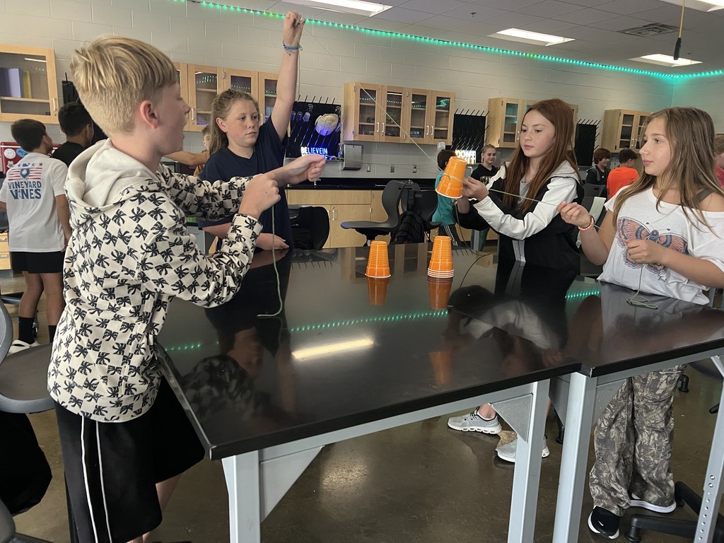 Students cooperate to stack cups using strings as part of a team-building exercise.