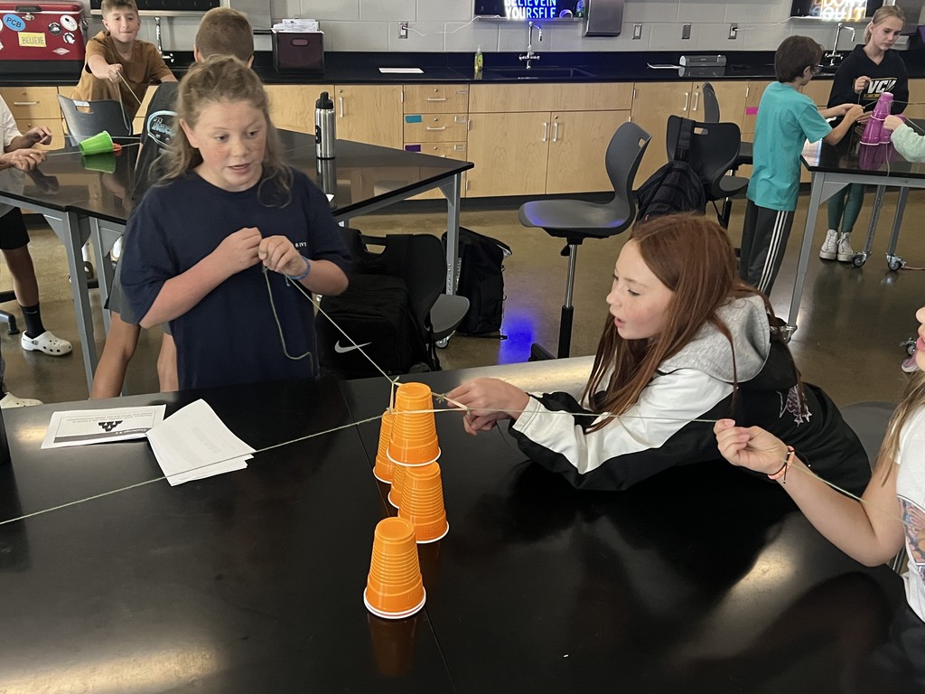 Students cooperate to stack cups using strings as part of a team-building exercise.