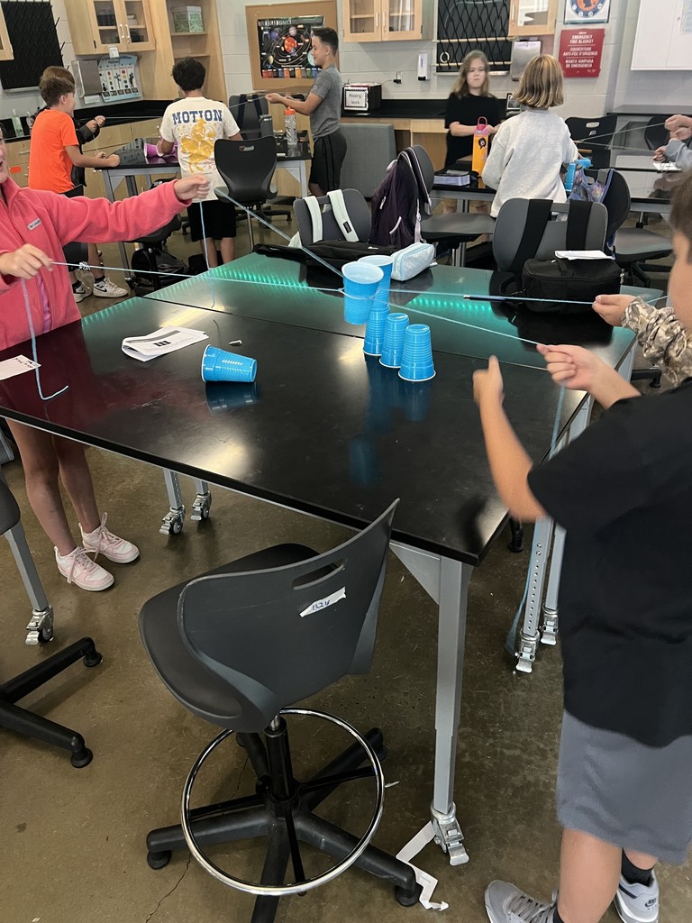 Students cooperate to stack cups using strings as part of a team-building exercise.