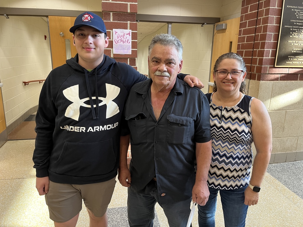 Two adults and a  student pose for a photo on a back-to-school night.