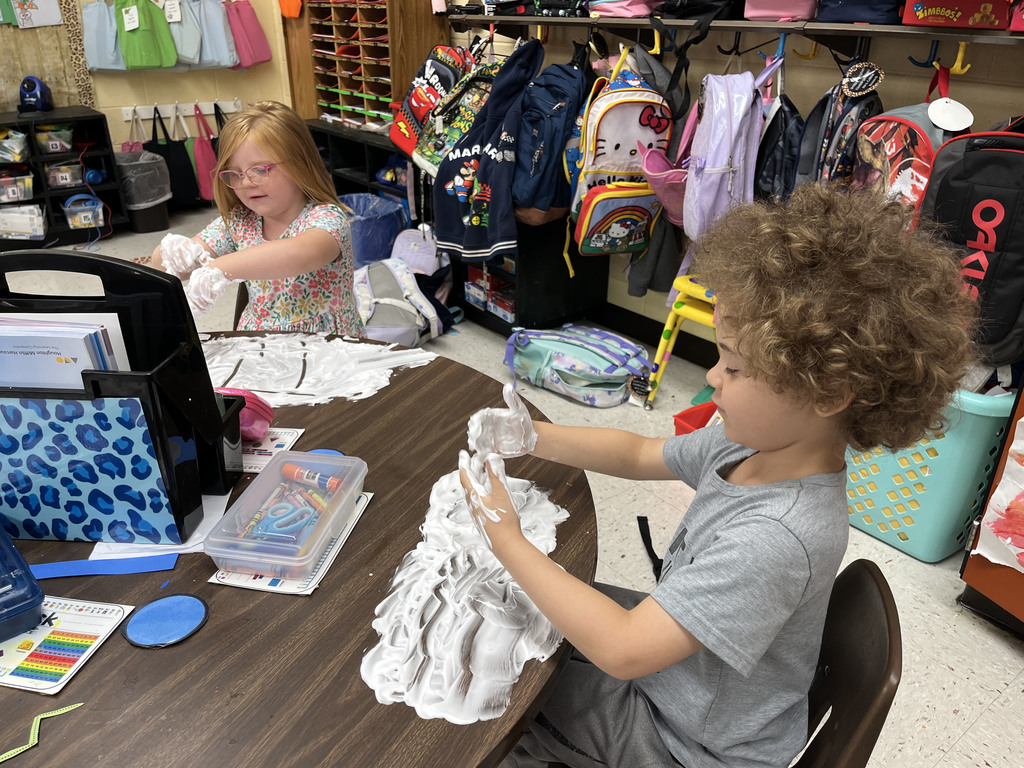 Students practice writing their letters using shaving cream on a desk. 