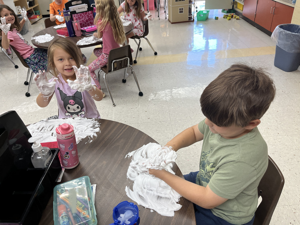 Students practice writing their letters using shaving cream on a desk. 