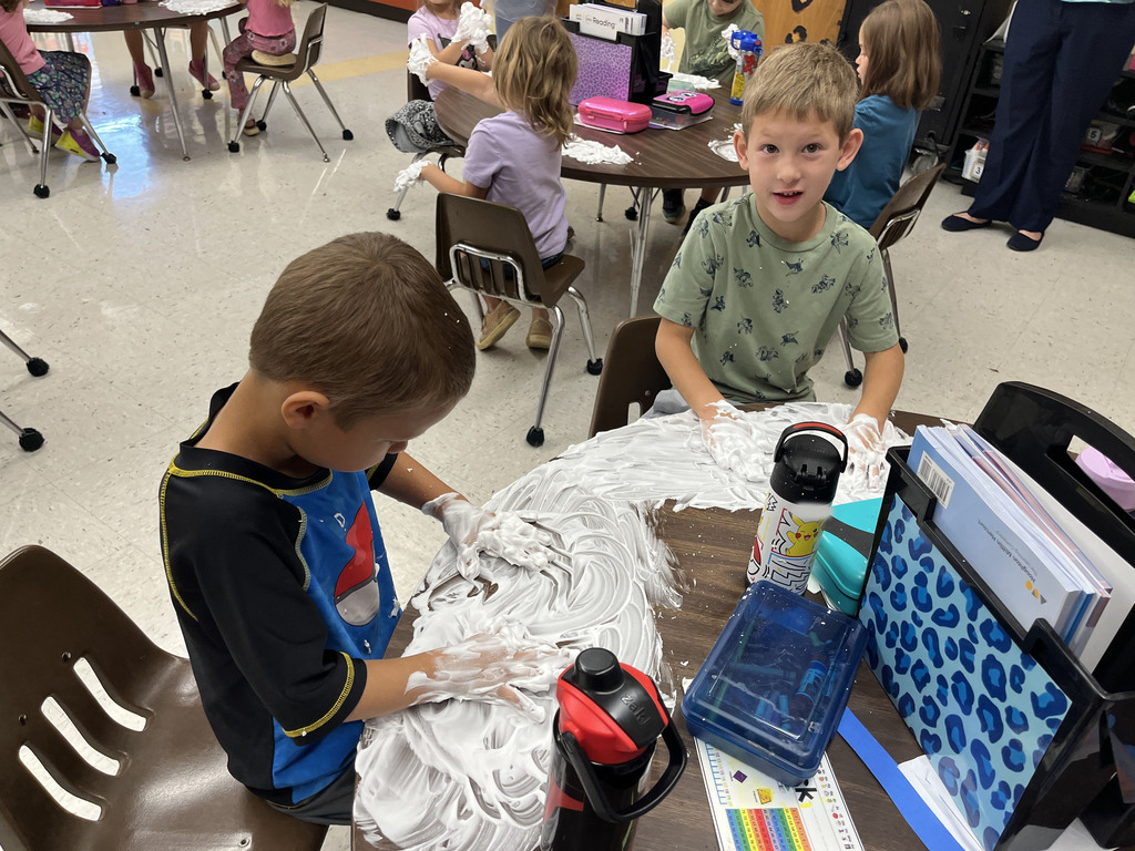 Students practice writing their letters using shaving cream on a desk. 
