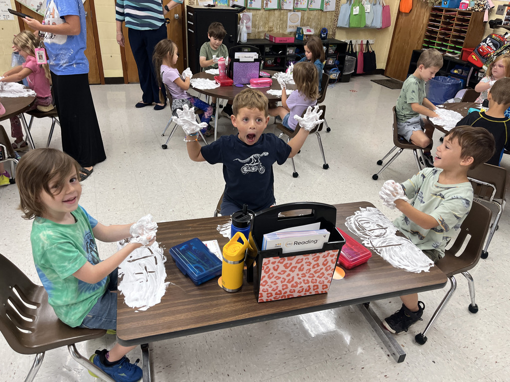 Students practice writing their letters using shaving cream on a desk. 