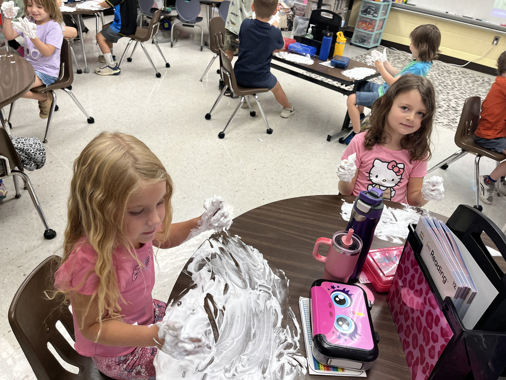Students practice writing their letters using shaving cream on a desk. 