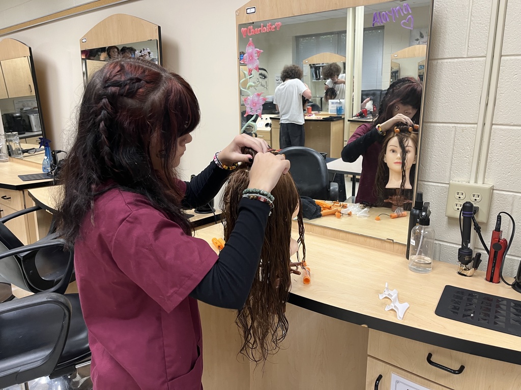 A student uses a cosmetology model head to practice perms. 