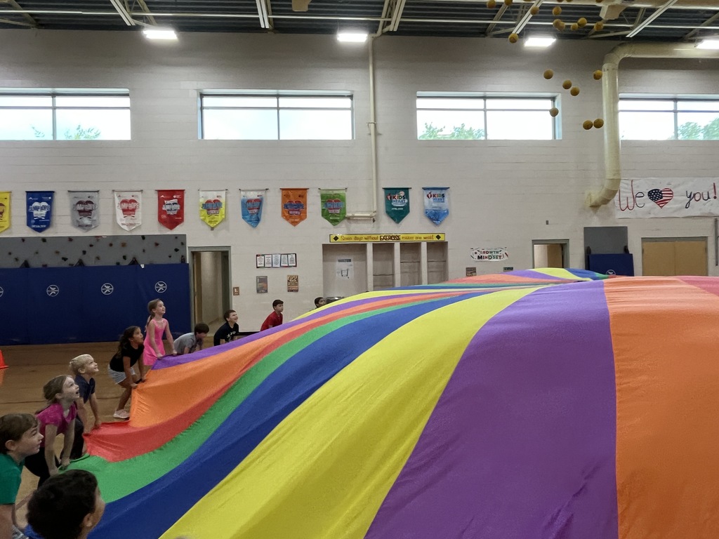 Students and their P.E. teachers play with a large rainbow parachute. 
