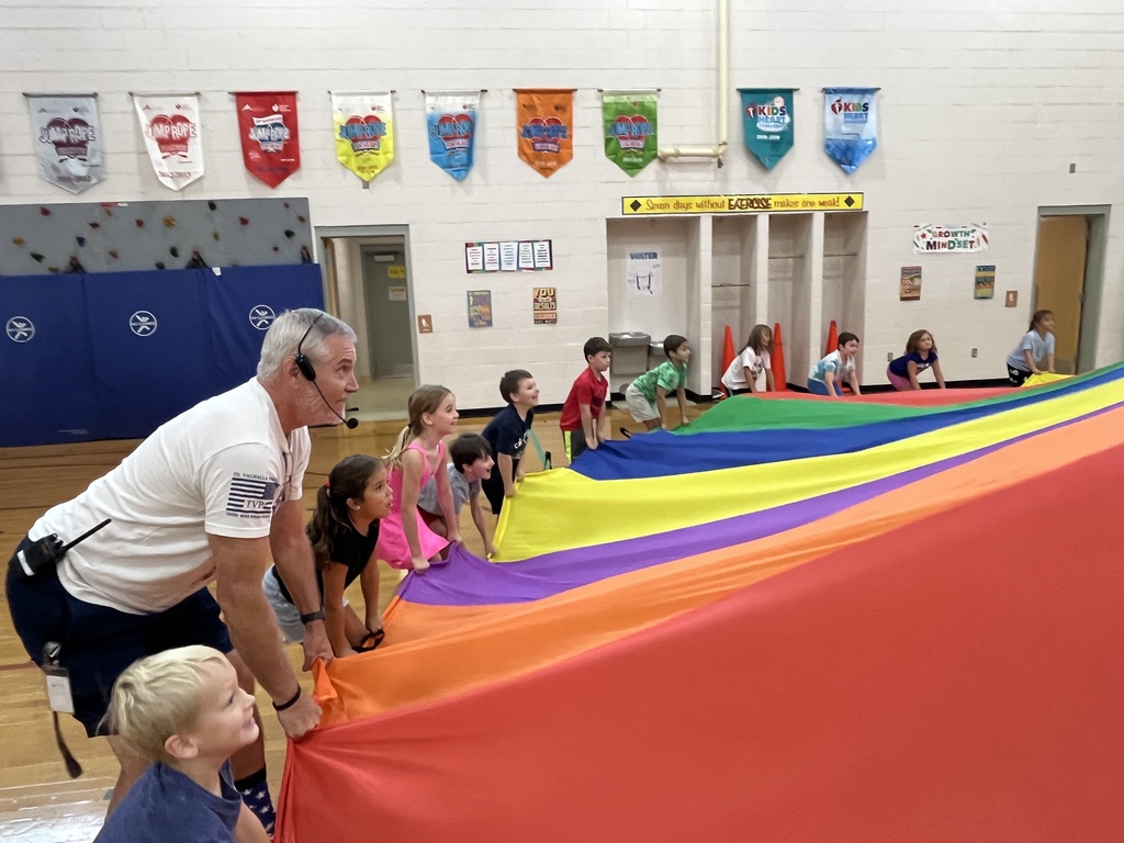 Students and their P.E. teachers play with a large rainbow parachute. 