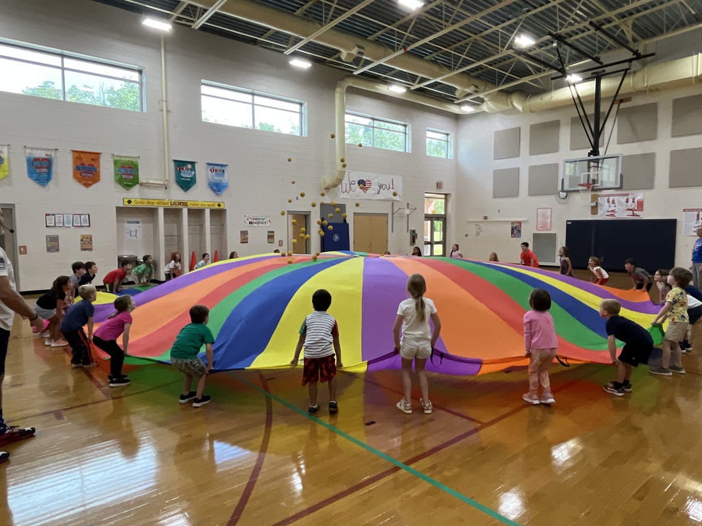 Students and their P.E. teachers play with a large rainbow parachute. 