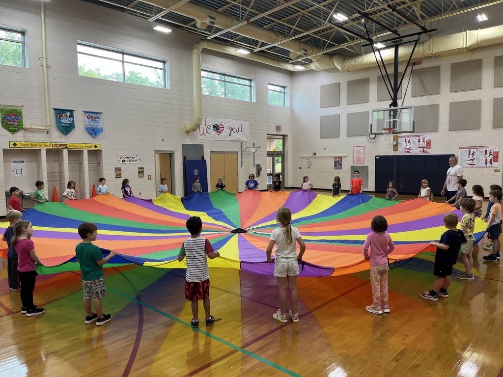 Students and their P.E. teachers play with a large rainbow parachute. 