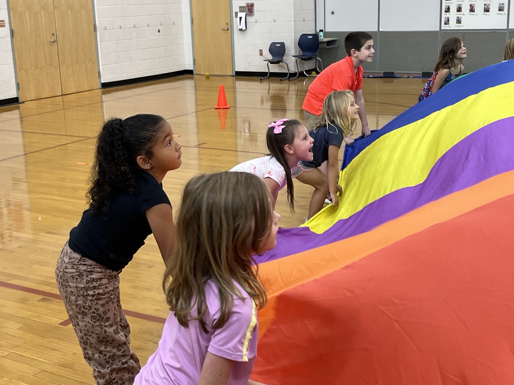 Students and their P.E. teachers play with a large rainbow parachute. 