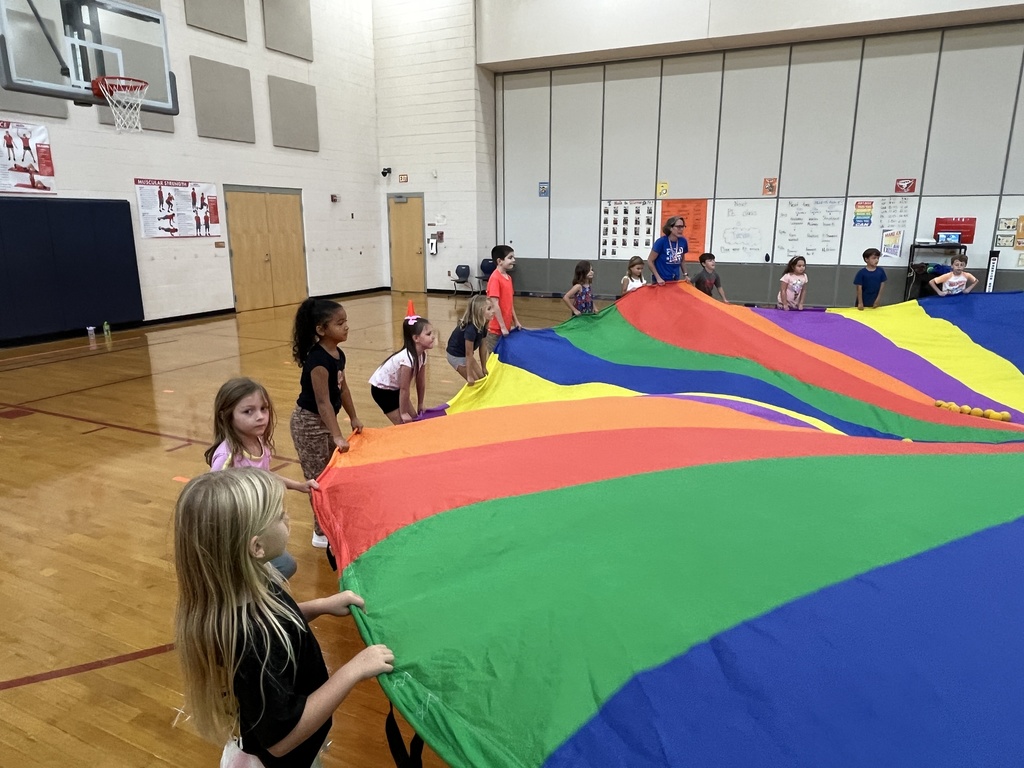 Students and their P.E. teachers play with a large rainbow parachute. 