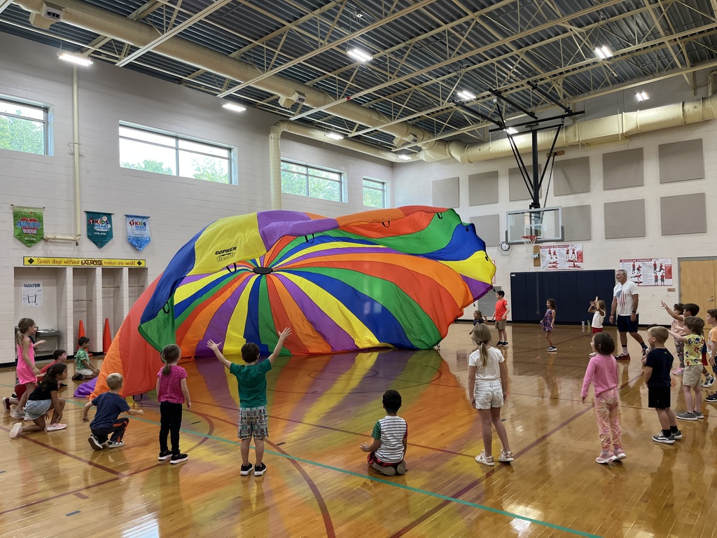 Students and their P.E. teachers play with a large rainbow parachute. 