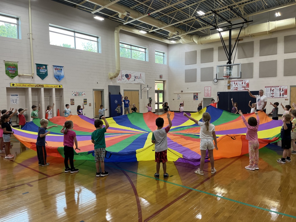 Students and their P.E. teachers play with a large rainbow parachute. 