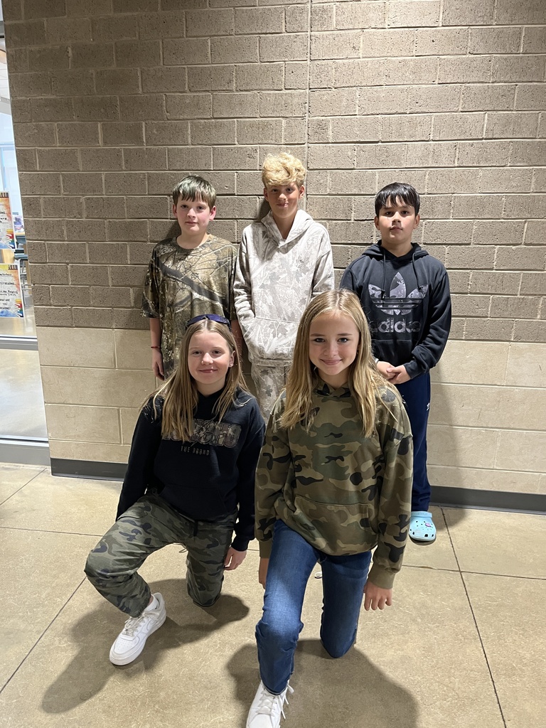 A small group of students pose for a photo showing off attire for Camo Day. 