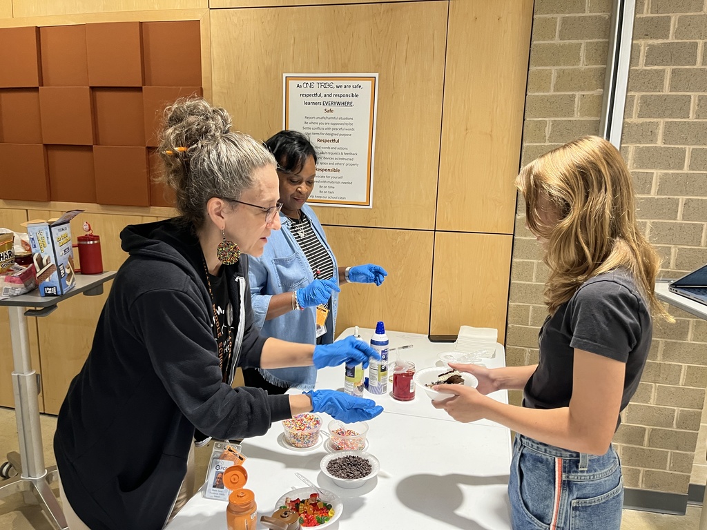 Two adults serve a student an ice cream sundae.