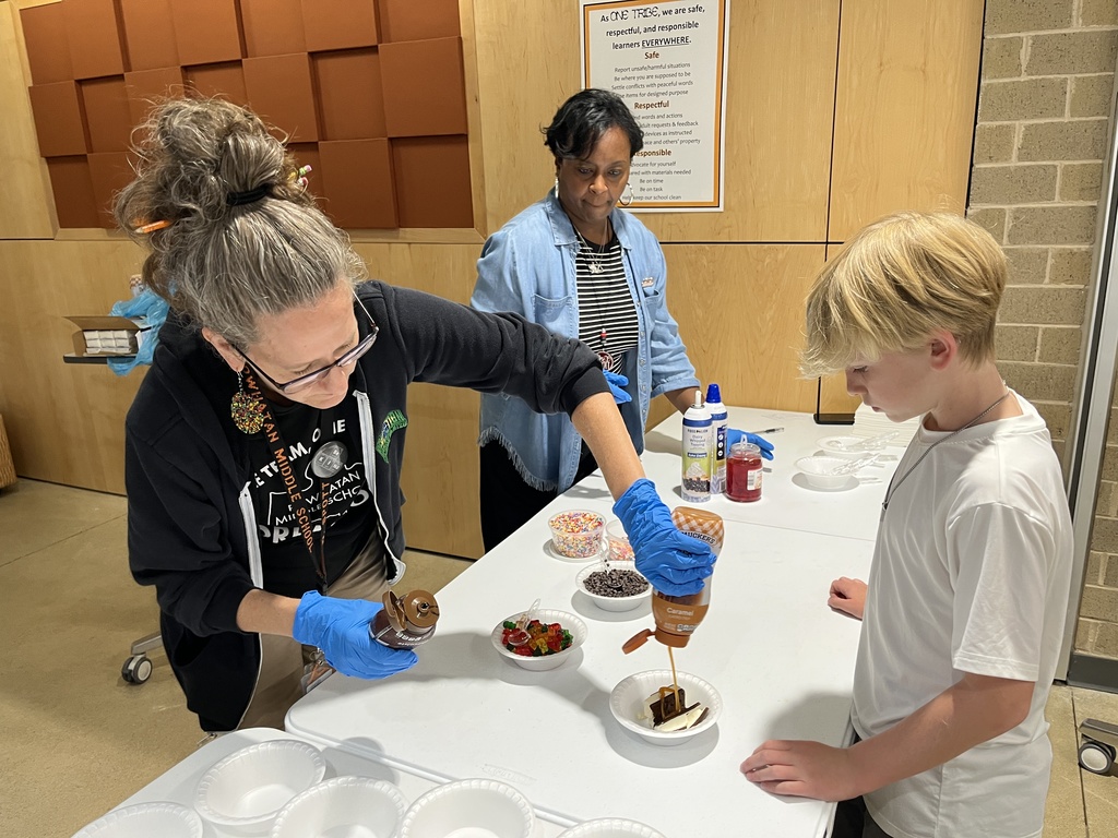 Two adults serve a student an ice cream sundae.