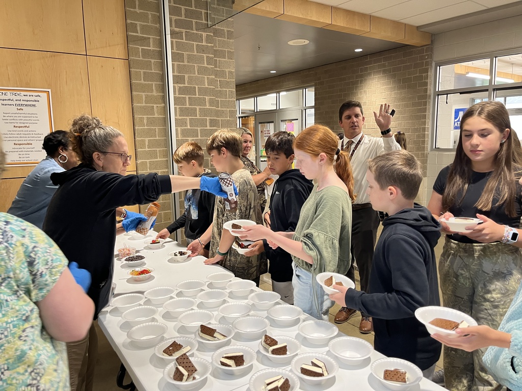 Two adults serve students ice cream sundaes.