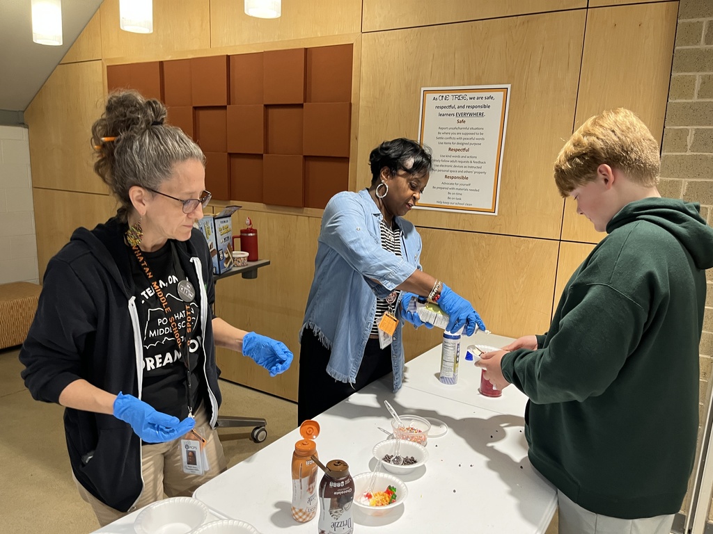 Two adults serve a student an ice cream sundae.