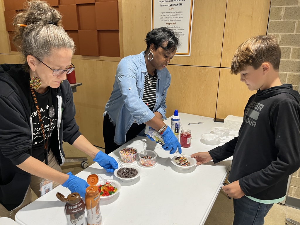 Two adults serve a student an ice cream sundae.
