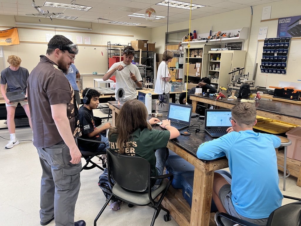 A teacher watches students build wind turbines. 