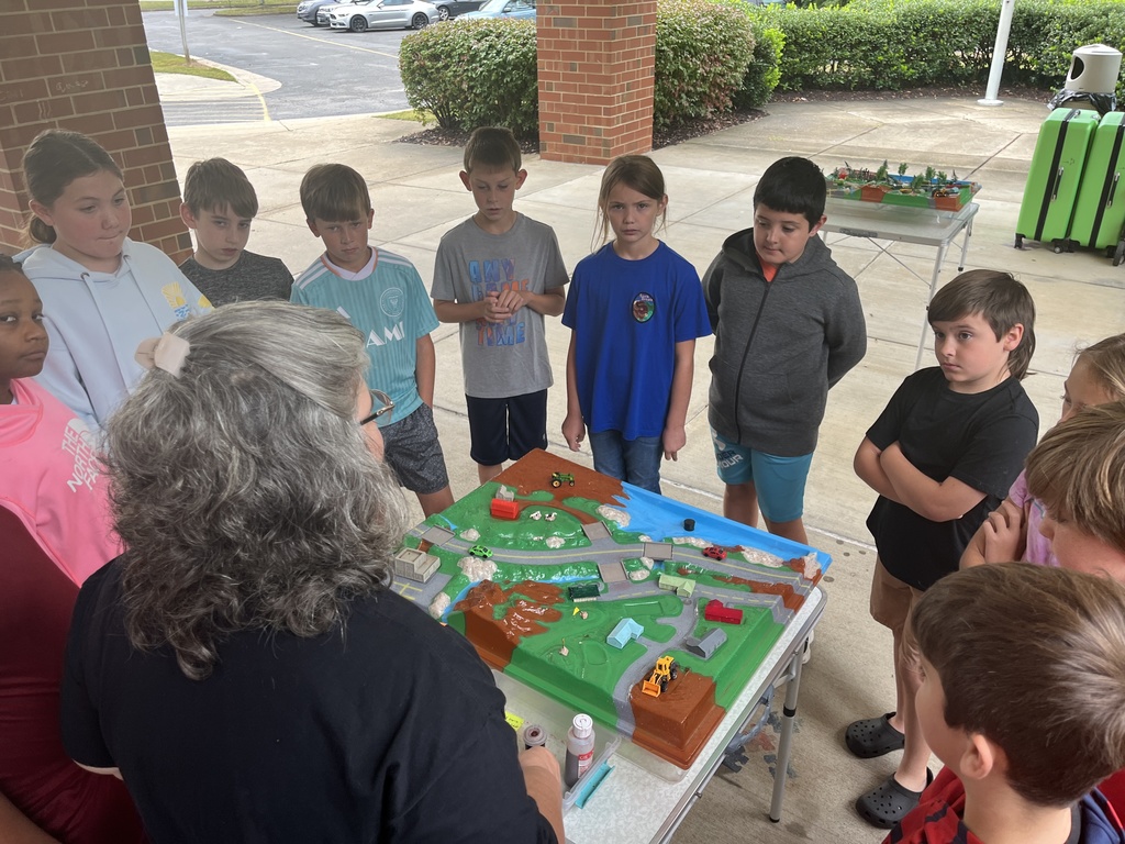 An adult uses a demonstration board to teach a group of students about watersheds.