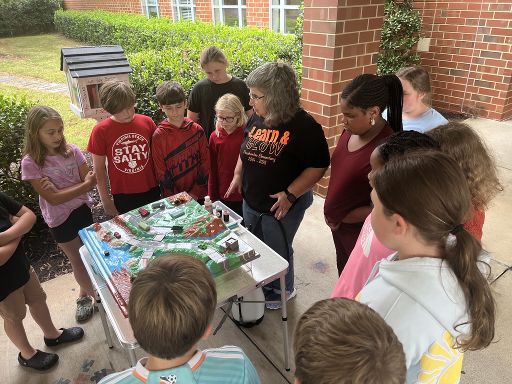 An adult uses a demonstration board to teach a group of students about watersheds.