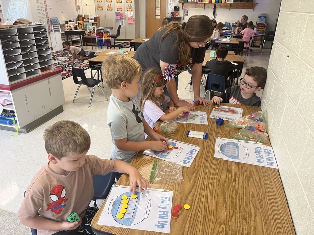 An adult helps kindergarteners working at a math station. 