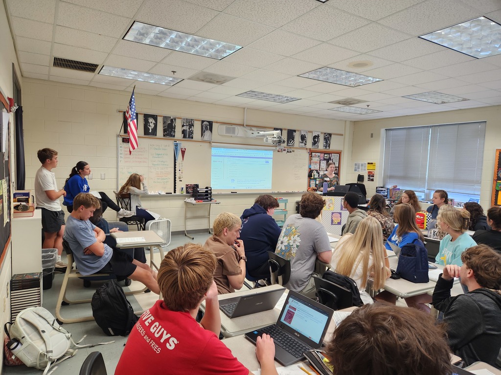 A woman at a podium speaks to a classroom full of students.