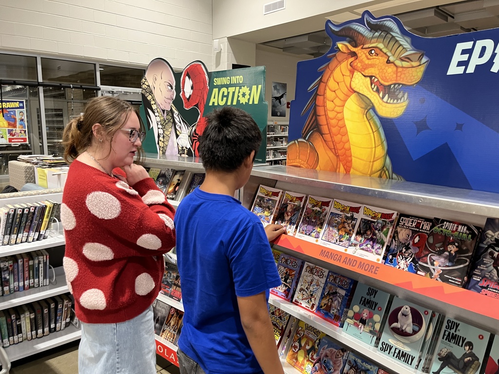 A student shops at a middle school book fair. and talks with a teacher.